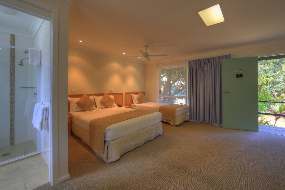 A hotel room with a large bed, a separate seating area, a shower, and a view of the outdoors.