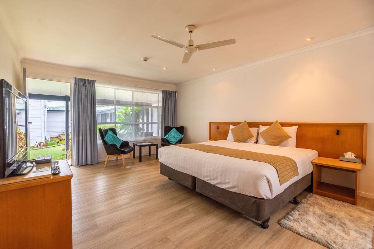 A hotel room with a large bed, a desk with a computer, a chair, and a view of the outside.