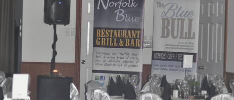 A restaurant interior with tables set for dining, hanging plants, and banners advertising the venue.