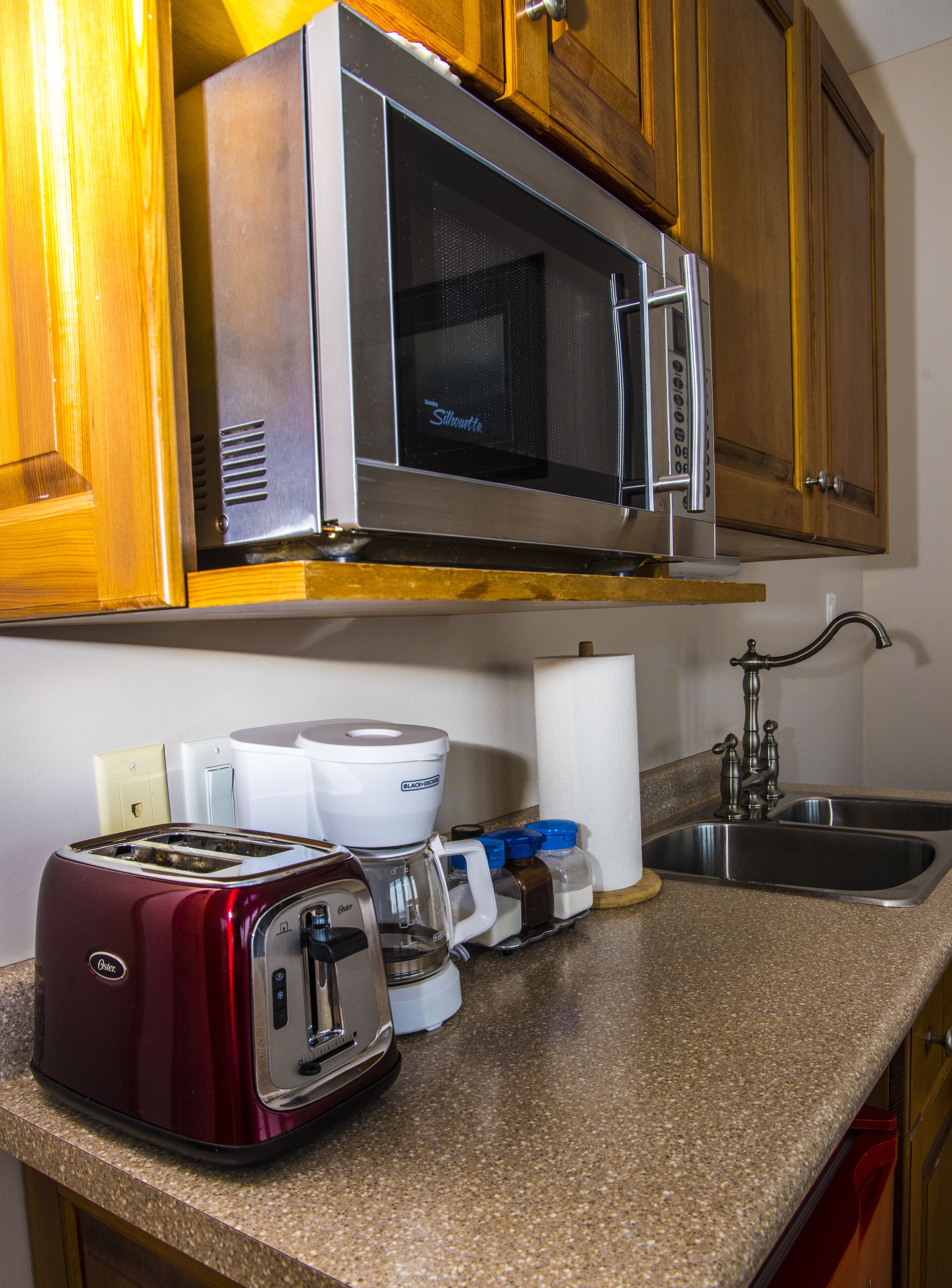 A kitchen with a microwave, toaster, coffee maker, and a sink.