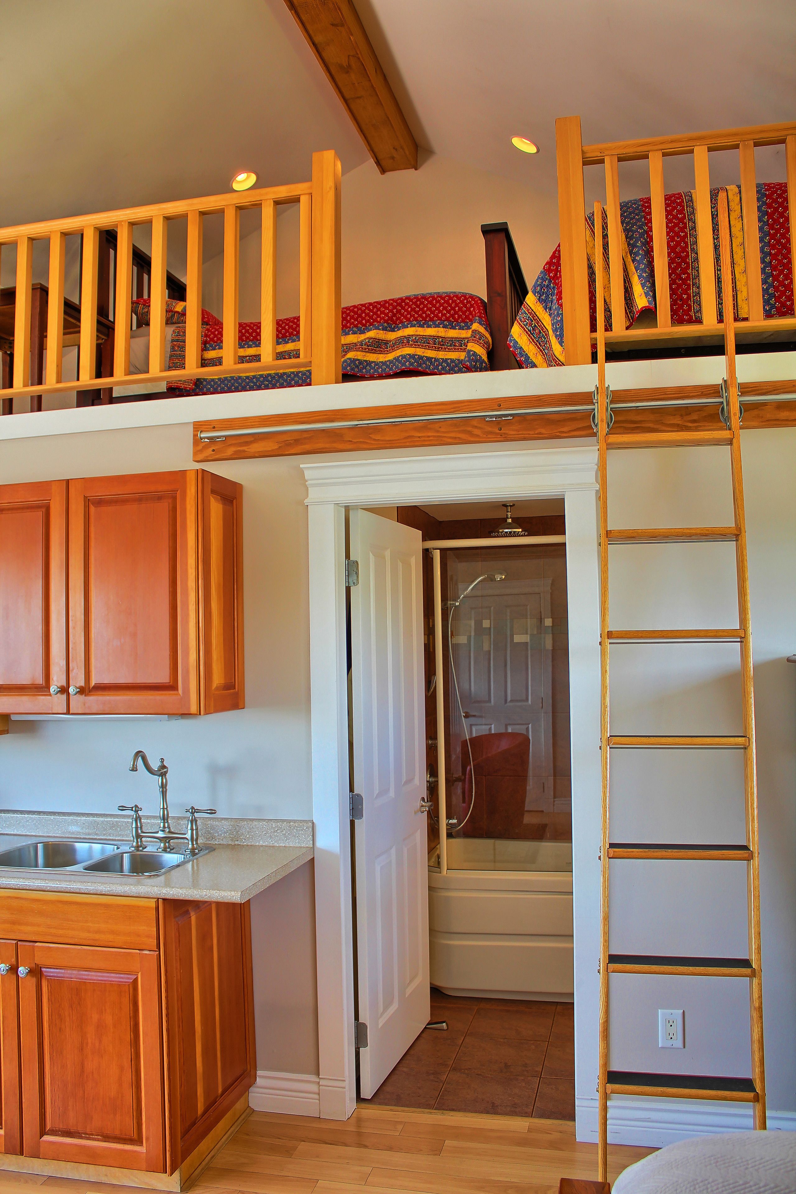 A loft bedroom with a bunk bed, wooden cabinets, a kitchen area, and a bathroom with a shower.