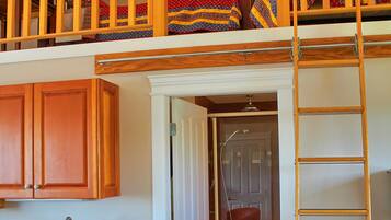 A loft bedroom with a bunk bed, wooden cabinets, a kitchen area, and a bathroom with a shower.