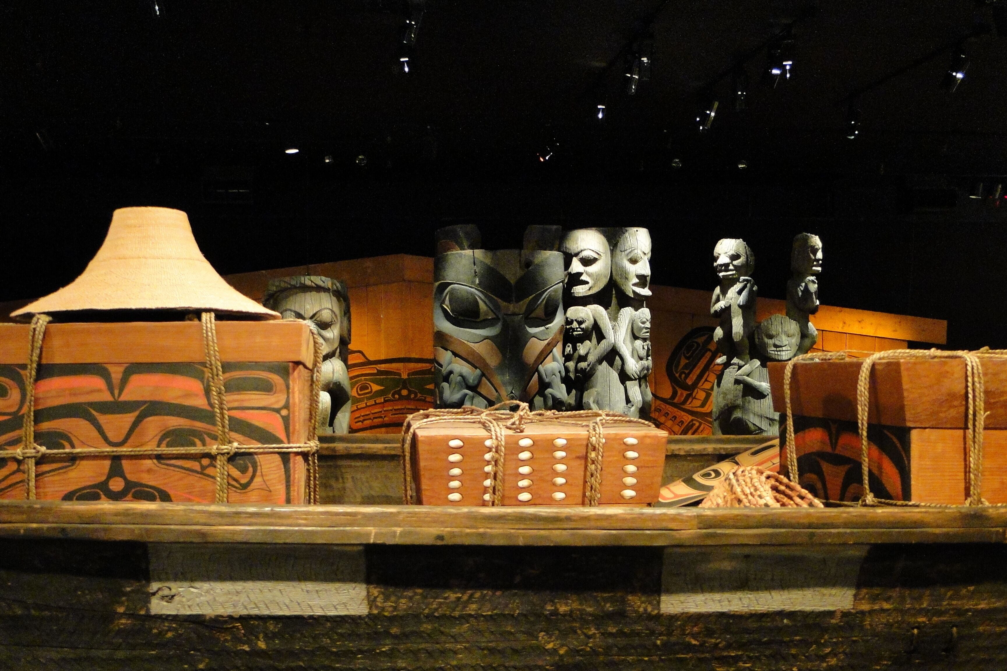 Een presentatie van traditionele artefacten, waaronder maskers en houten kisten, op een donkere achtergrond.
