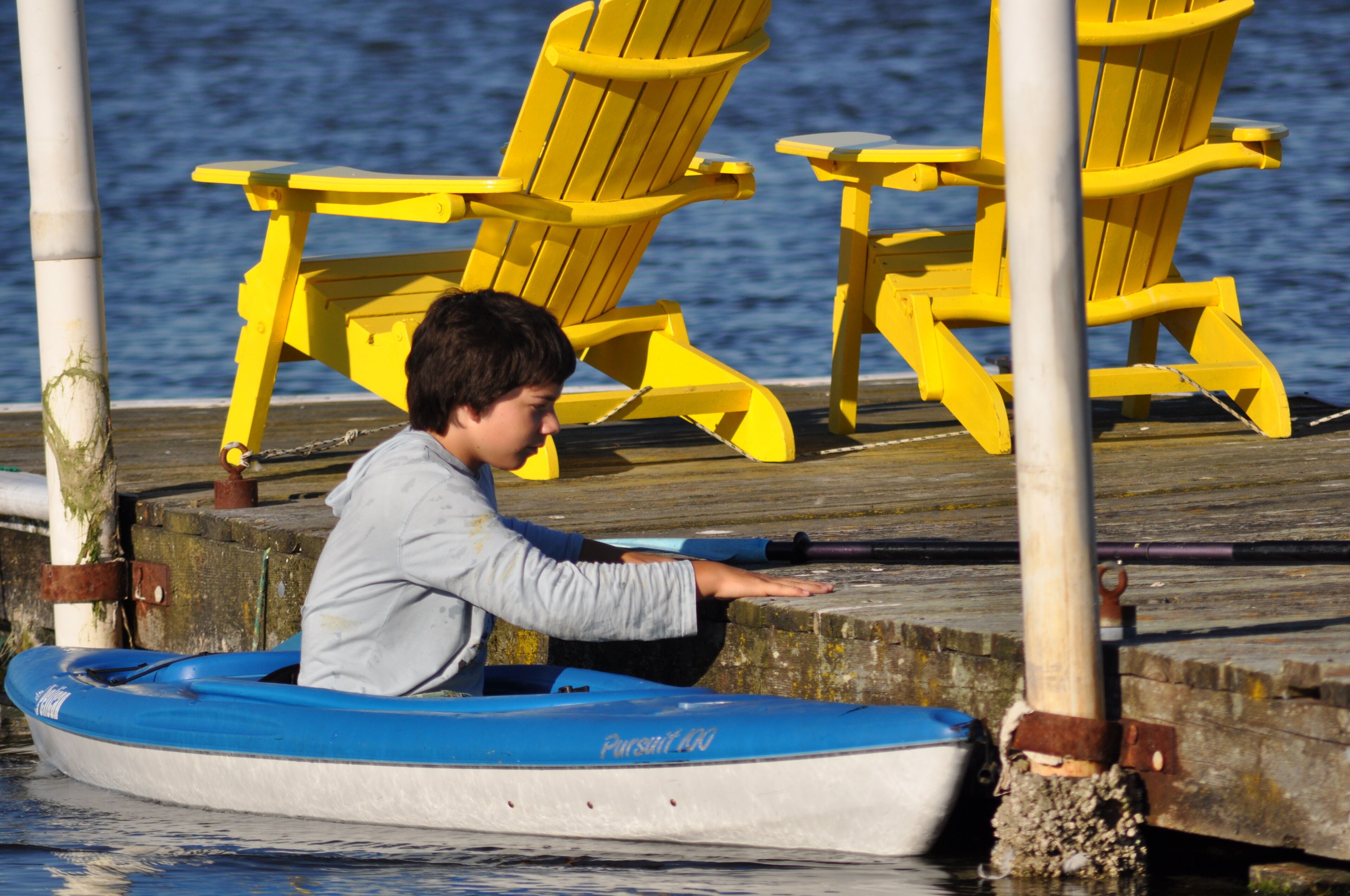Una persona en un kayak azul sobre un muelle con sillas y mesas amarillas.