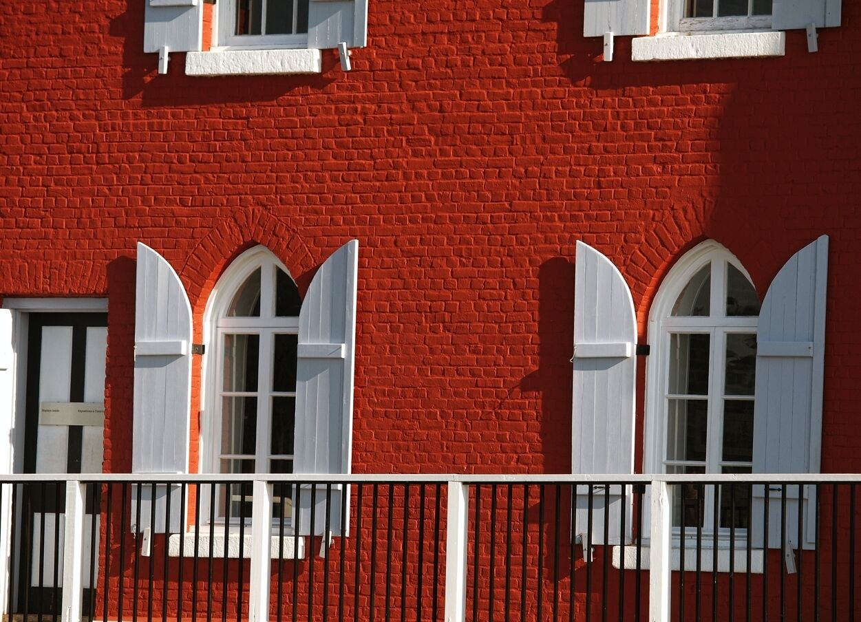 Ein roter Backsteinbau mit weiß gefassten Fenstern und einem weißen Zaun im Vordergrund.