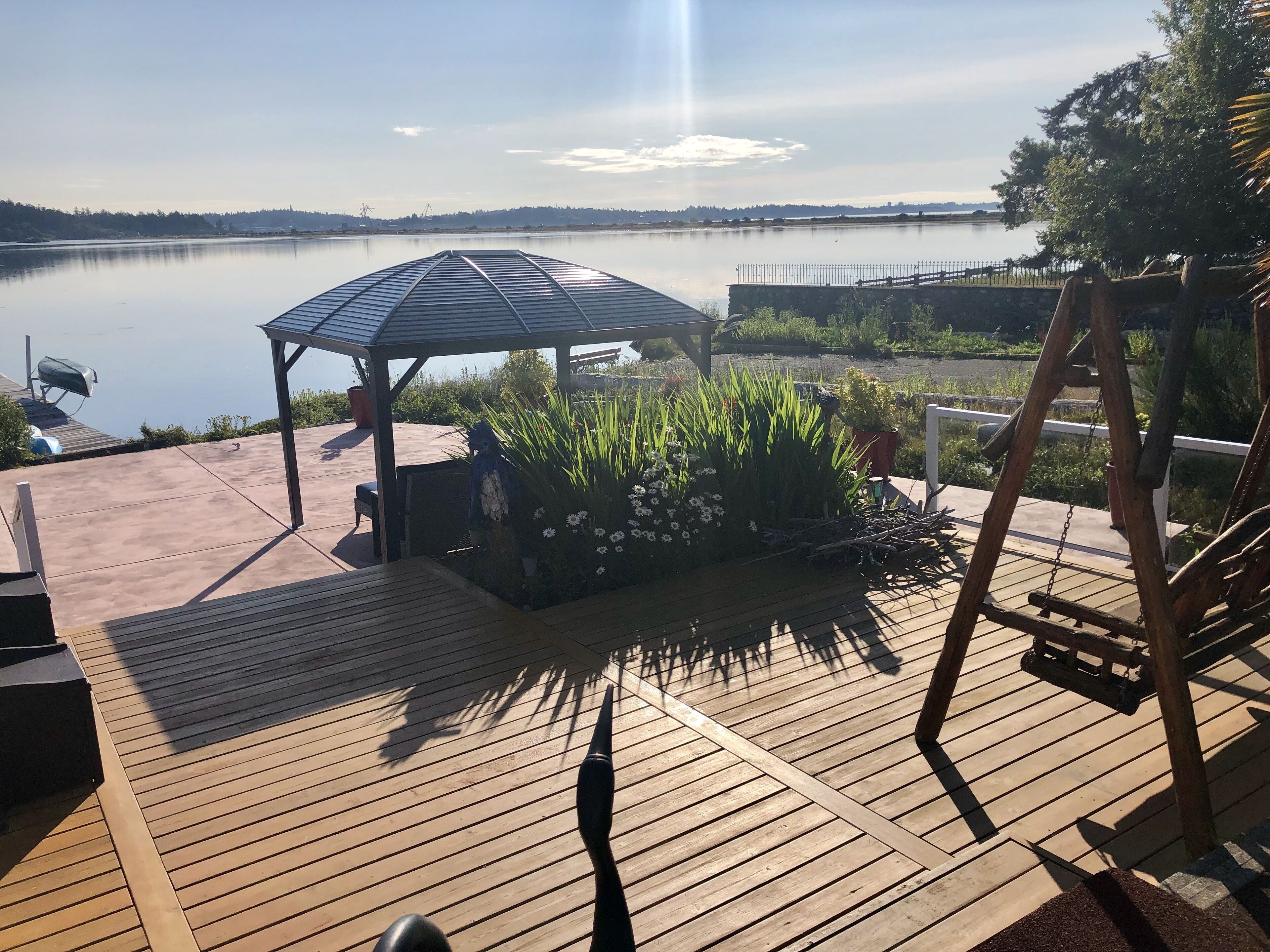 A wooden deck with a gazebo, a swing set, and a view of a calm lake.