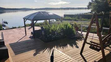 A wooden deck with a gazebo, a swing set, and a view of a calm lake.