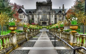 A grand stone building with a symmetrical facade, a central entrance, and a formal garden with flower beds and urns. - Birds of a Feather Victoria Oceanfront Studio Suites (Victoria)