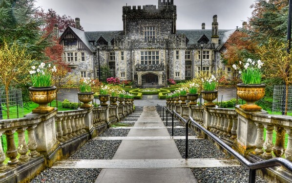 A grand stone building with a symmetrical facade, a central entrance, and a formal garden with flower beds and urns. - Birds of a Feather Victoria Oceanfront Studio Suites (Victoria)