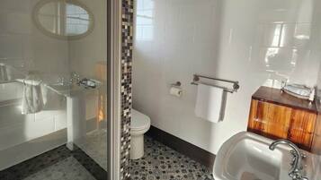 Un baño con cabina de ducha de vidrio, inodoro blanco, lavamanos con tocador de madera y baldosas de suelo estampadas.