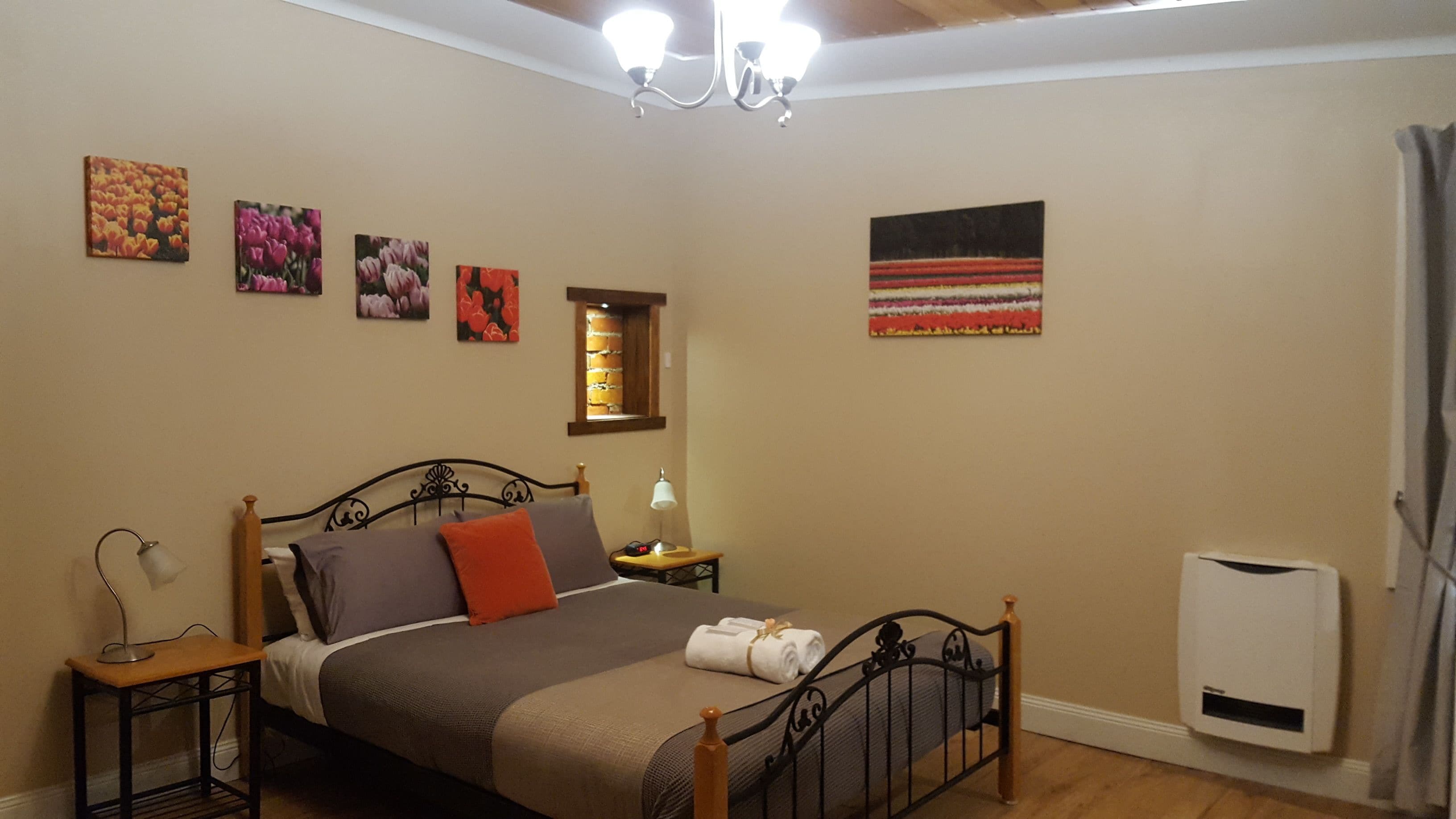 A bedroom with a bed, a bedside table, a lamp, a heater, and four wall-mounted paintings.