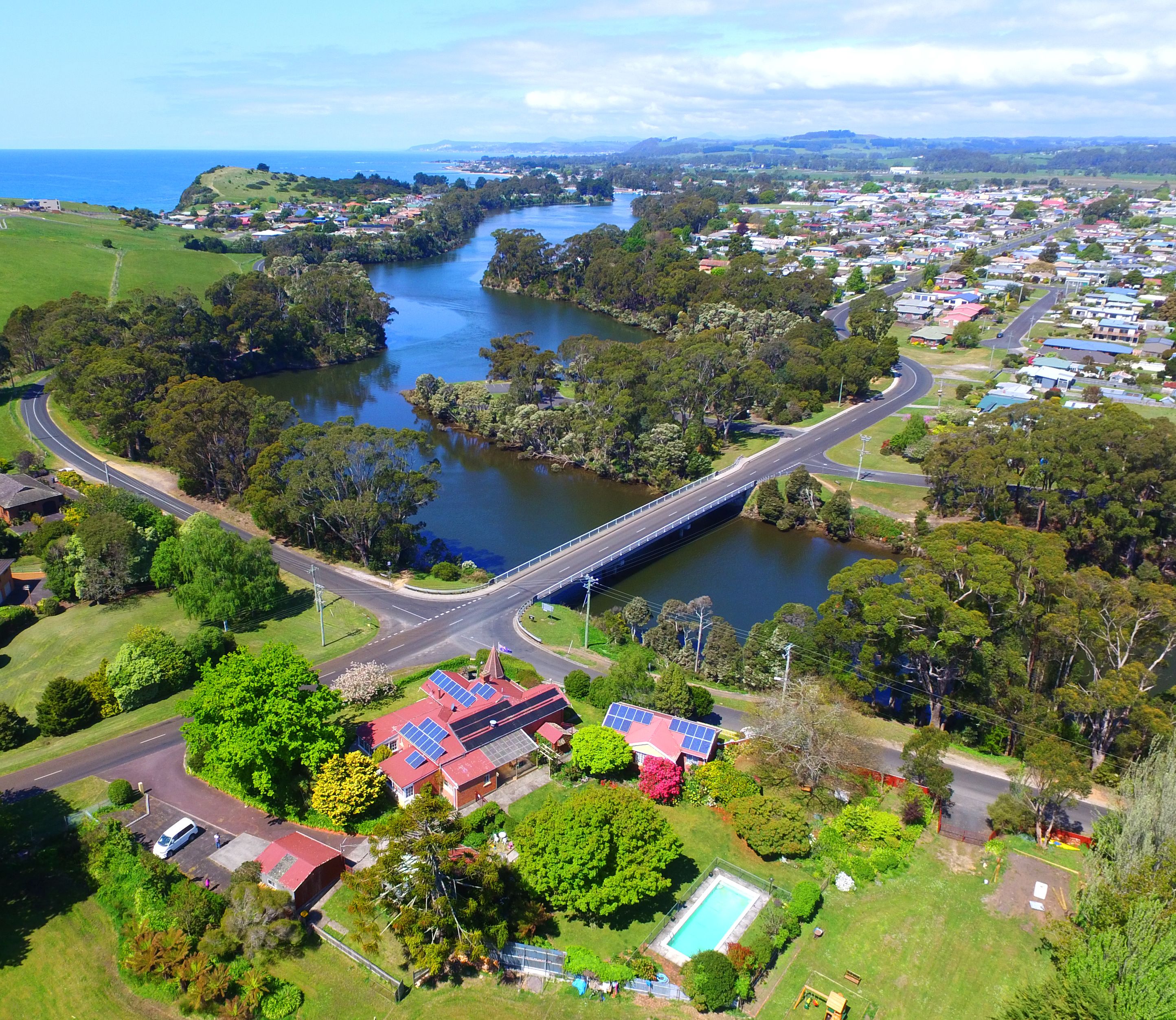 An aerial view of a coastal town with a prominent bridge, green spaces, and residential areas.