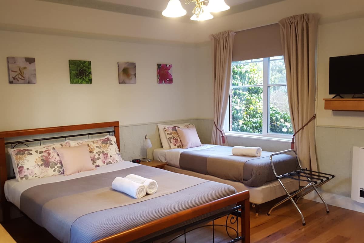 A hotel room with two beds, a desk, a chair, a TV, and a window with curtains.