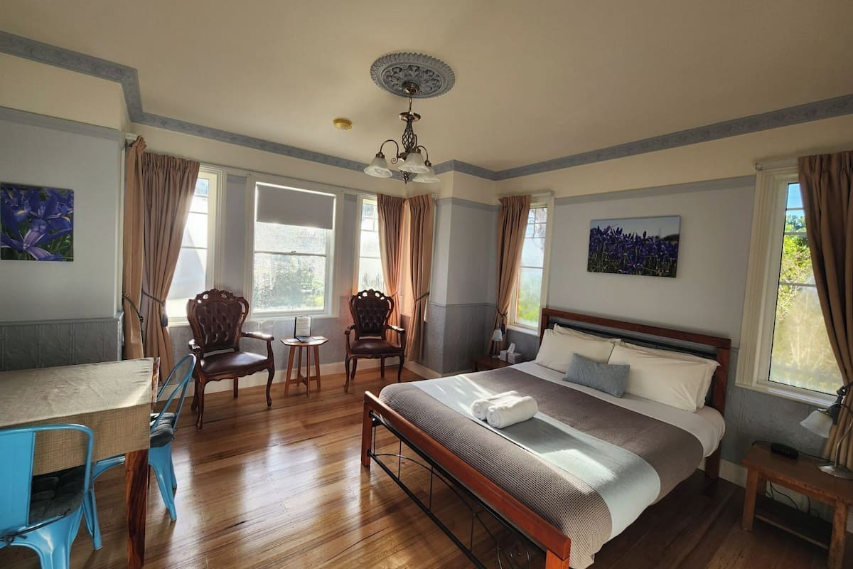 A bedroom with a bed, two chairs, a table, and a ceiling fan.