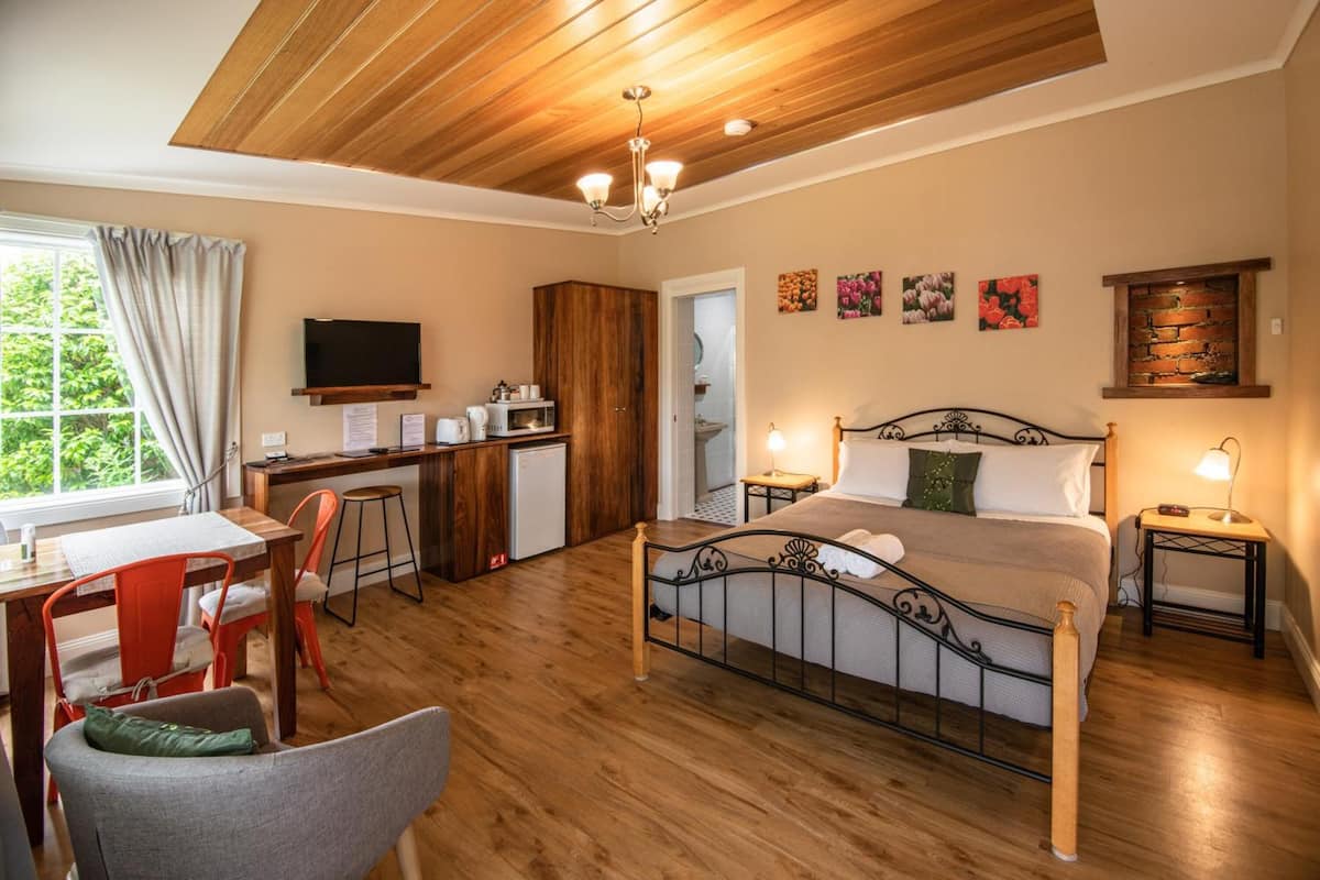A bedroom with a wooden ceiling, a bed with a metal frame, a desk with a TV, and a window with curtains.