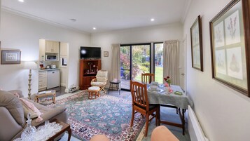 A living room with a sofa, a dining table with chairs, a TV, and a kitchen area with a microwave.