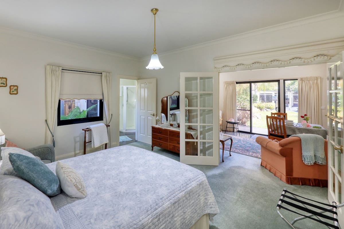Un dormitorio con cama, cómoda, televisión y balcón con mesa y sillas.