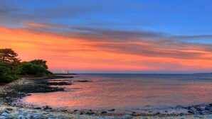 Un paisaje costero con costa rocosa y mar tranquilo bajo un cielo al atardecer.