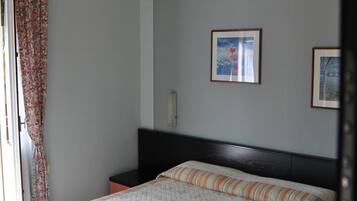 Un dormitorio con cama, mesita de noche, ventana con cortinas y dos cuadros en la pared.