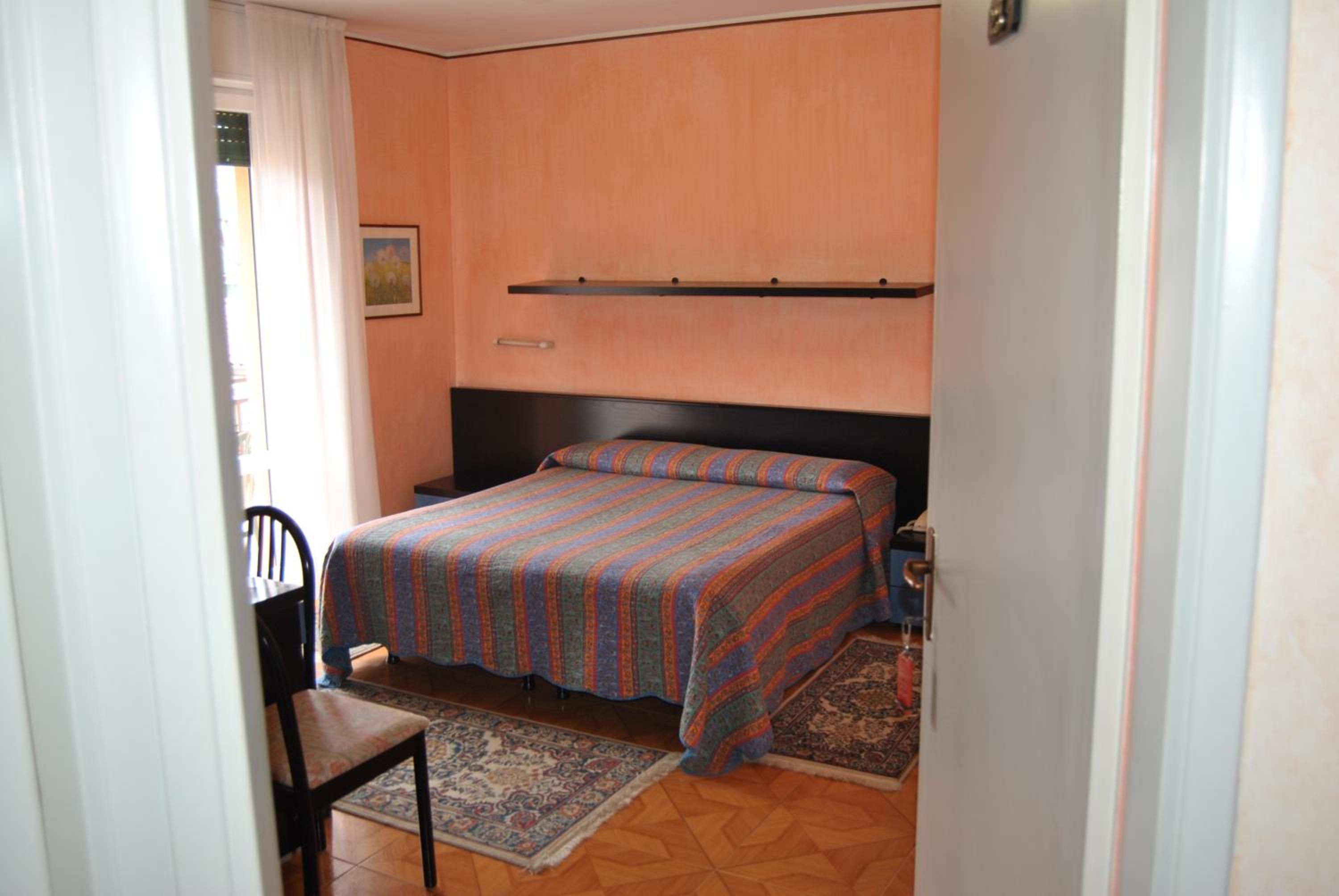 A small, single-bed room with a wooden headboard, a bedside table, a chair, and a rug on the floor.
