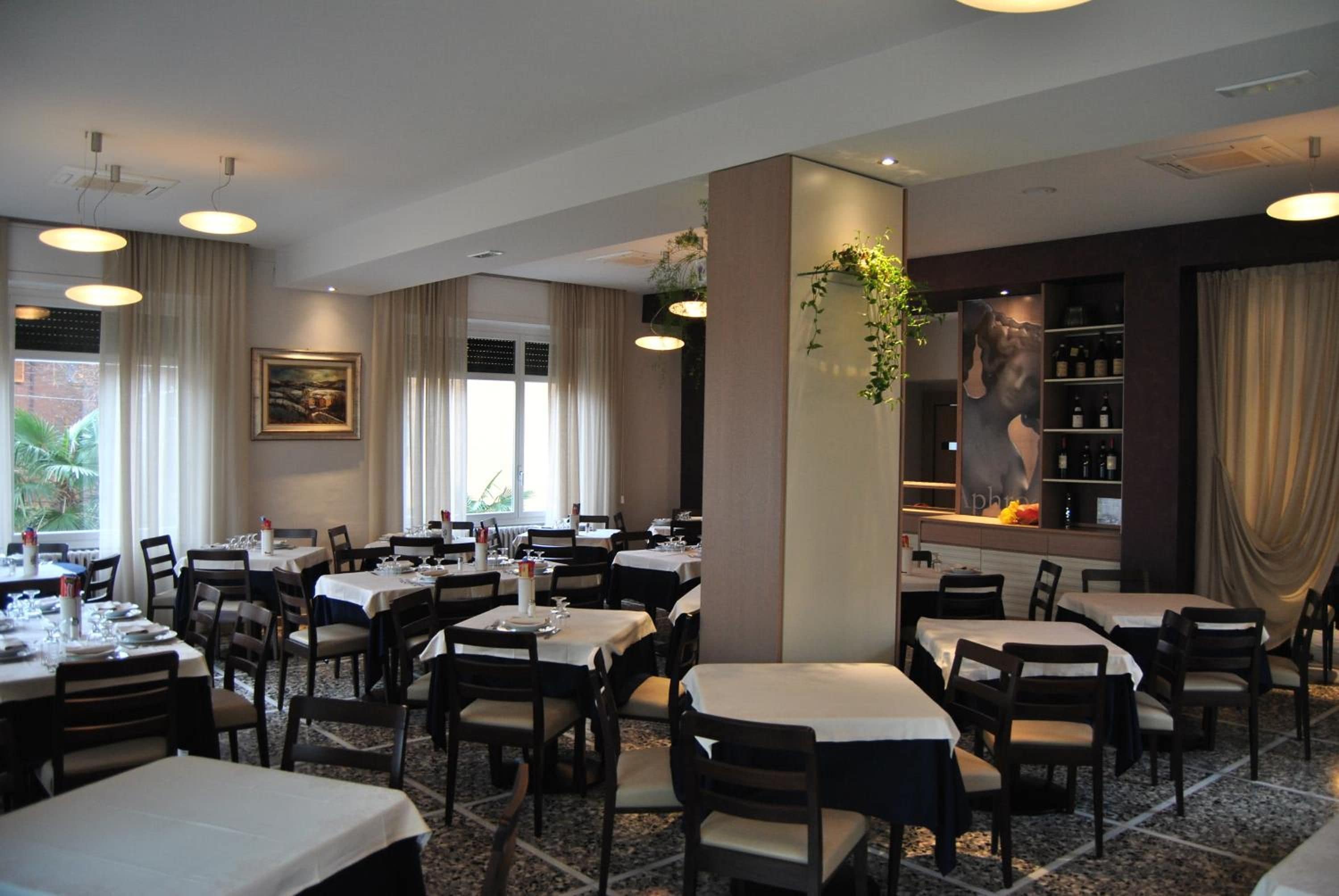 Un restaurant doté de nombreuses tables et chaises, d’un bar avec un présentoir à bouteilles de vin et d’un grand tableau accroché au mur.