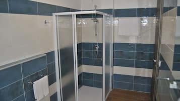 Une douche avec une porte en verre, un sol en bois et des carreaux bleus et blancs sur les murs.