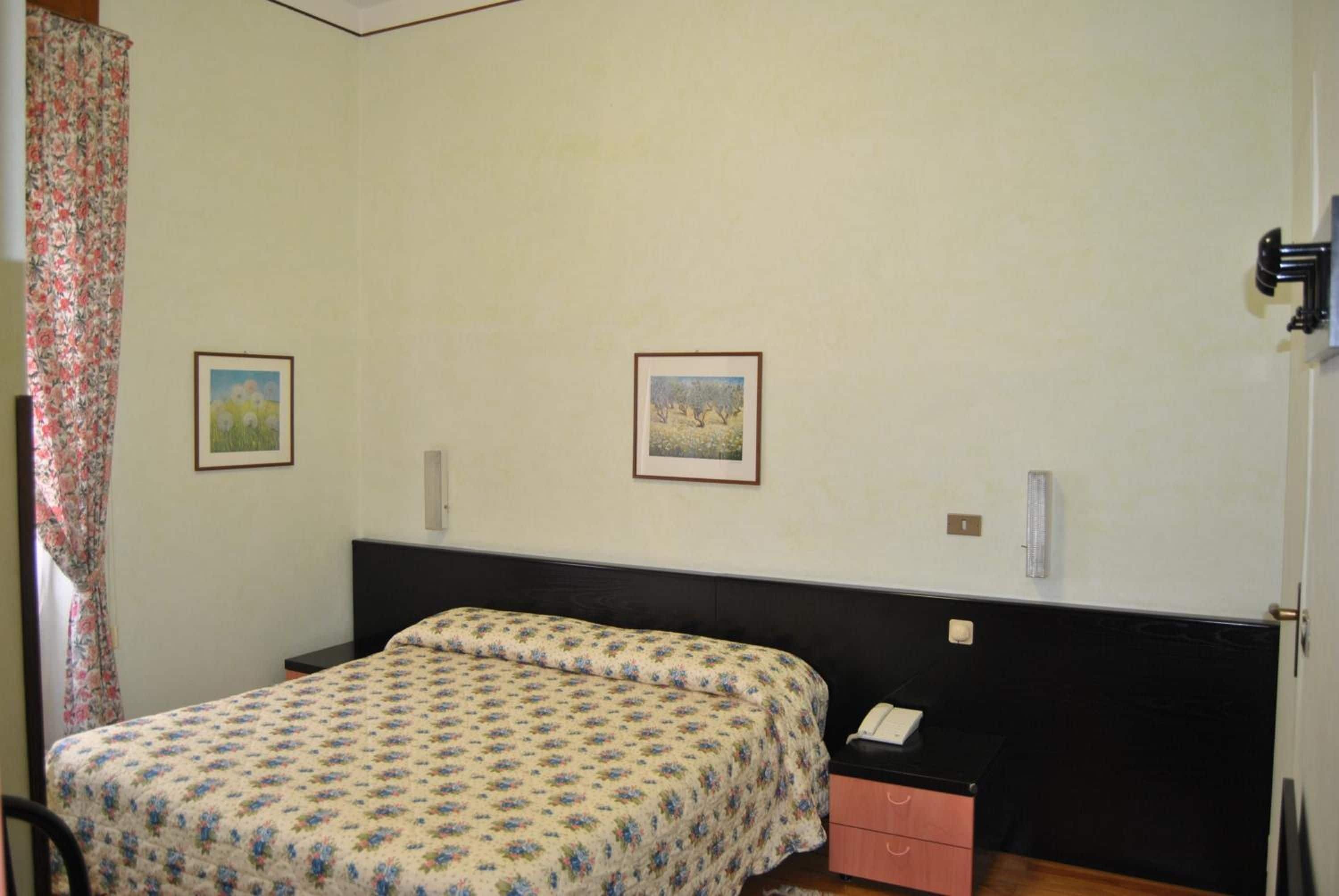A bedroom with a bed, a nightstand, two framed pictures on the wall, and a door with a handle.