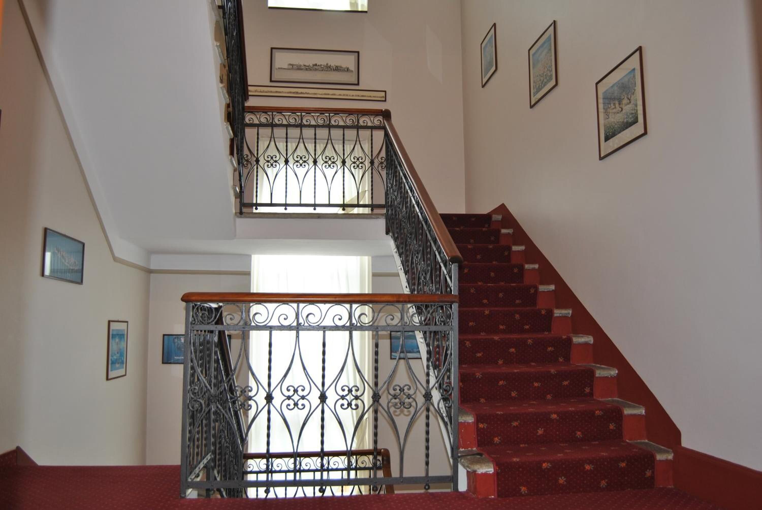 Eine Treppe mit roten Teppichstufen und einem schmiedeeisernen Geländer.