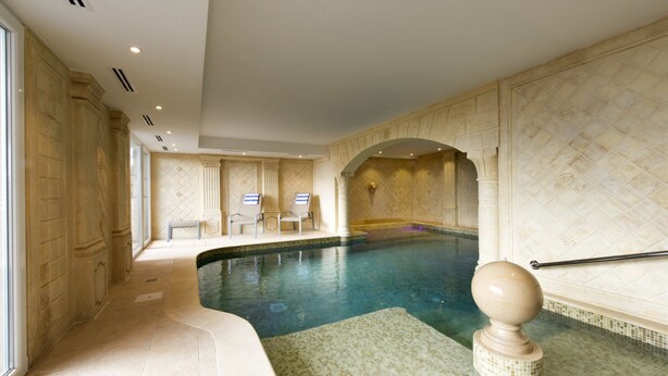 A luxurious indoor swimming pool with a tiled floor, a decorative balustrade, and a seating area with two chairs. - L'Alexain Hôtel Restaurant & Wellness (Niedermorschwihr)