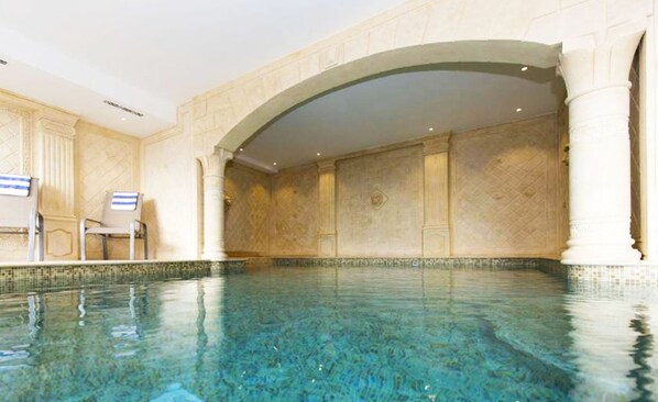 Una amplia piscina cubierta con agua cristalina, rodeada por un muro de azulejos con un diseño geométrico.