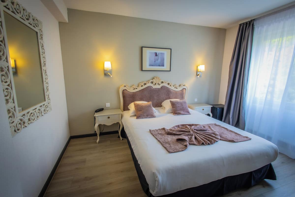 Habitación de hotel con una cama grande, dos mesitas de noche, un espejo y un cuadro en la pared.