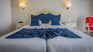 A neatly made bed with a blue blanket and pillows, two bedside tables with lamps, and a red chair. - L'Alexain Hôtel Restaurant & Wellness (Niedermorschwihr)