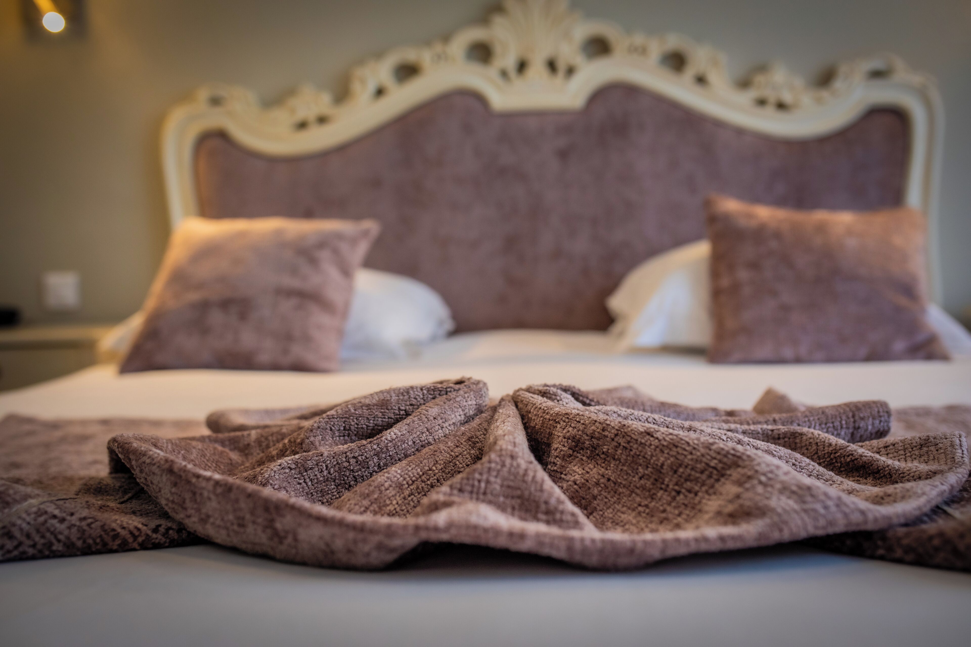 Een bed met een wit hoofdeinde, twee kussens, een bruine deken en een witte lakens.