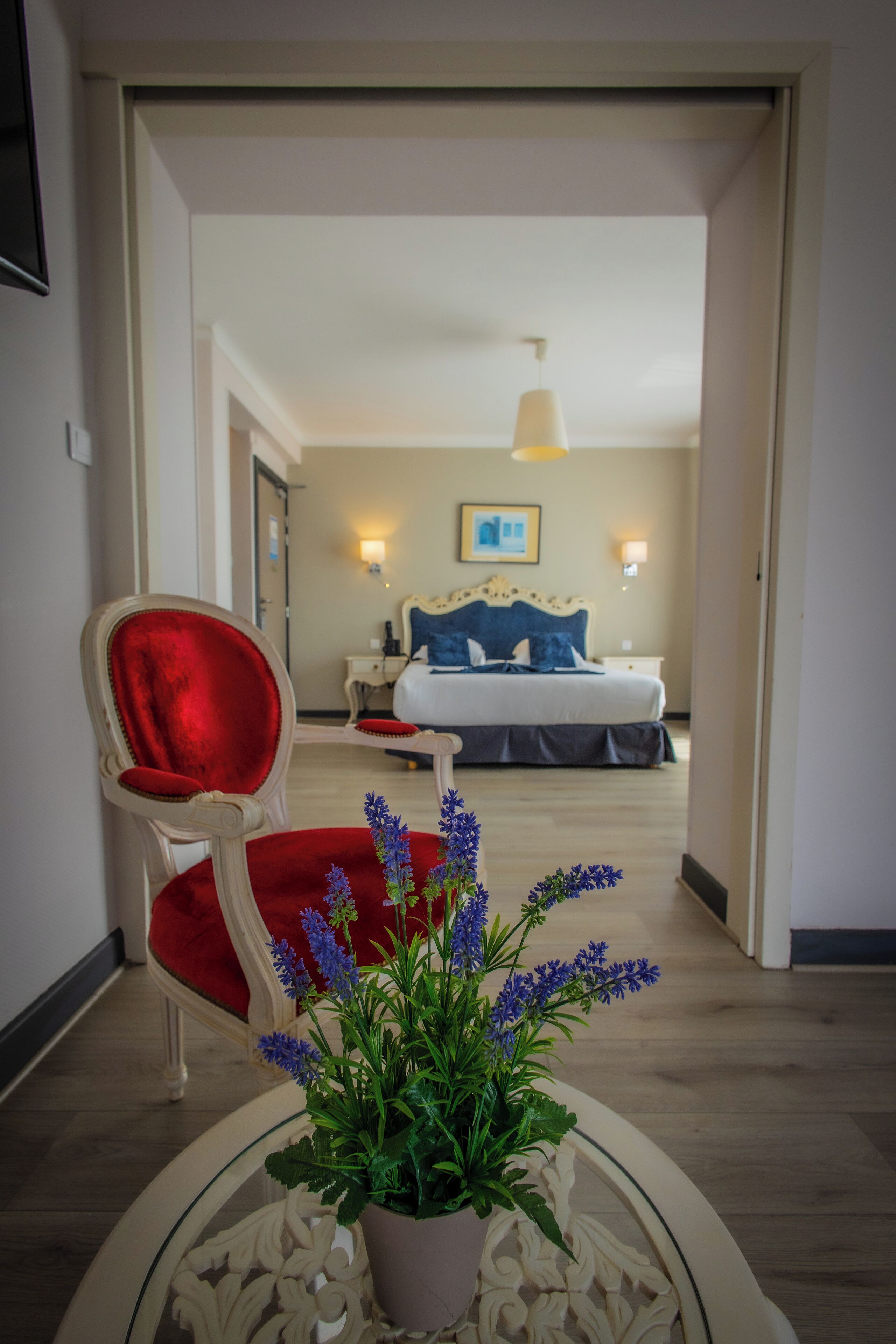 A hotel room with a bed, bedside tables, a lamp, and a chair with a red cushion.
