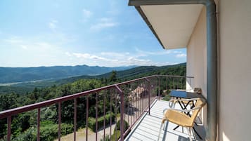 A balcony with a view of mountains, a table, and two chairs.