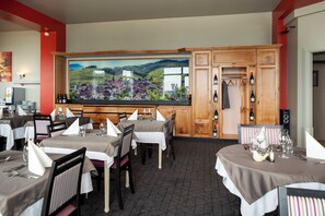 Un restaurante con varias mesas dispuestas para comer, un cuadro grande de un paisaje en la pared y una estantería con botellas de vino.