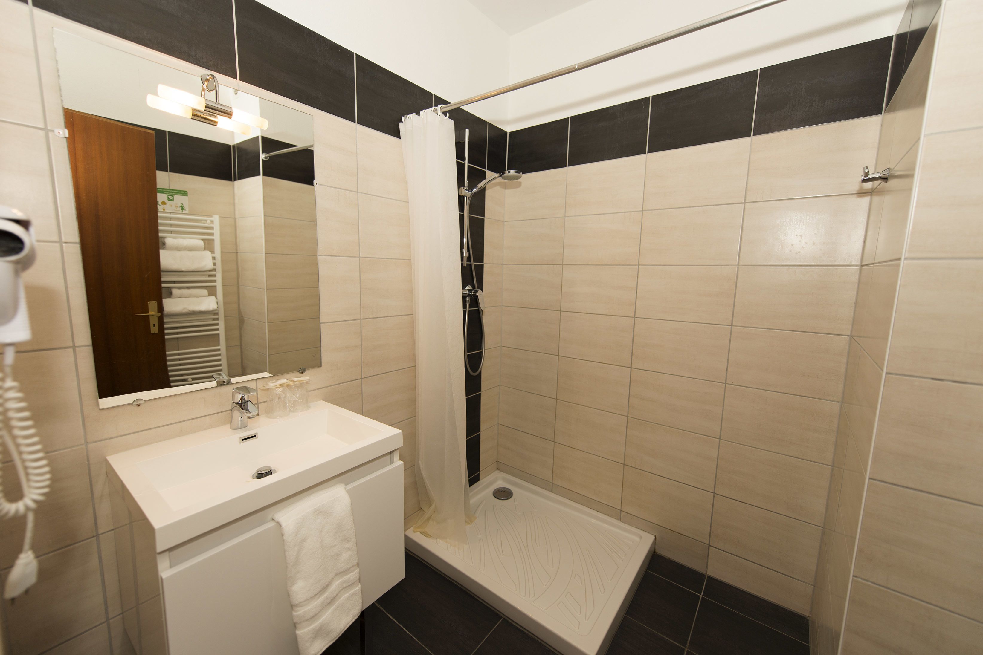 A bathroom with a white sink, a mirror, a shower with a curtain, and a towel rack with towels.