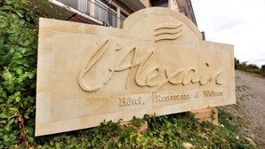 A sign for 'L'Alexain Hotel, Restaurant & Wellness' with a stylized sun and wave design. - L'Alexain Hôtel Restaurant & Wellness (Niedermorschwihr)
