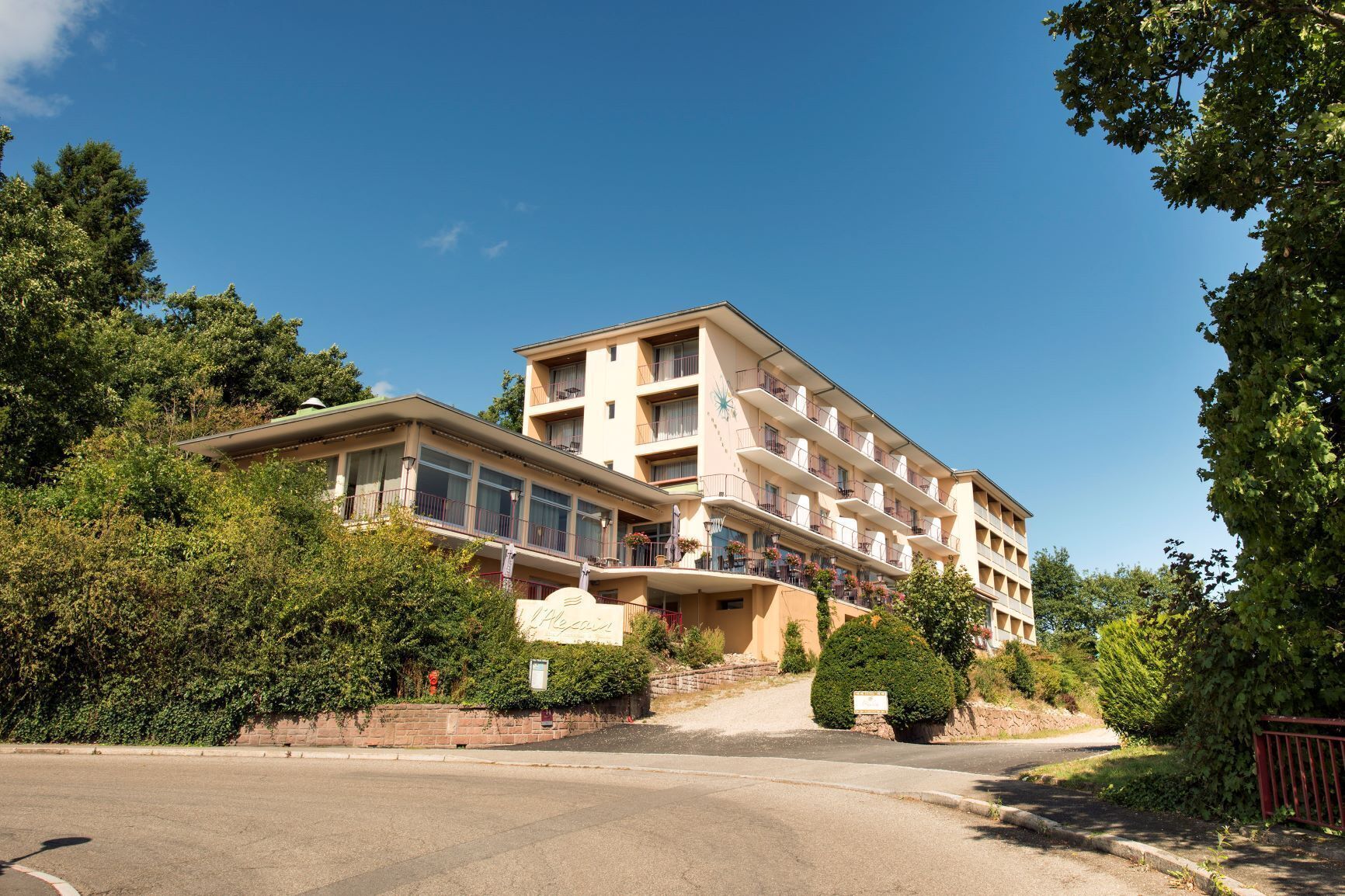 A multi-story hotel with balconies, surrounded by greenery and a clear sky.