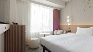 A hotel room with a bed, a desk, a chair, a small table, and a window with curtains.