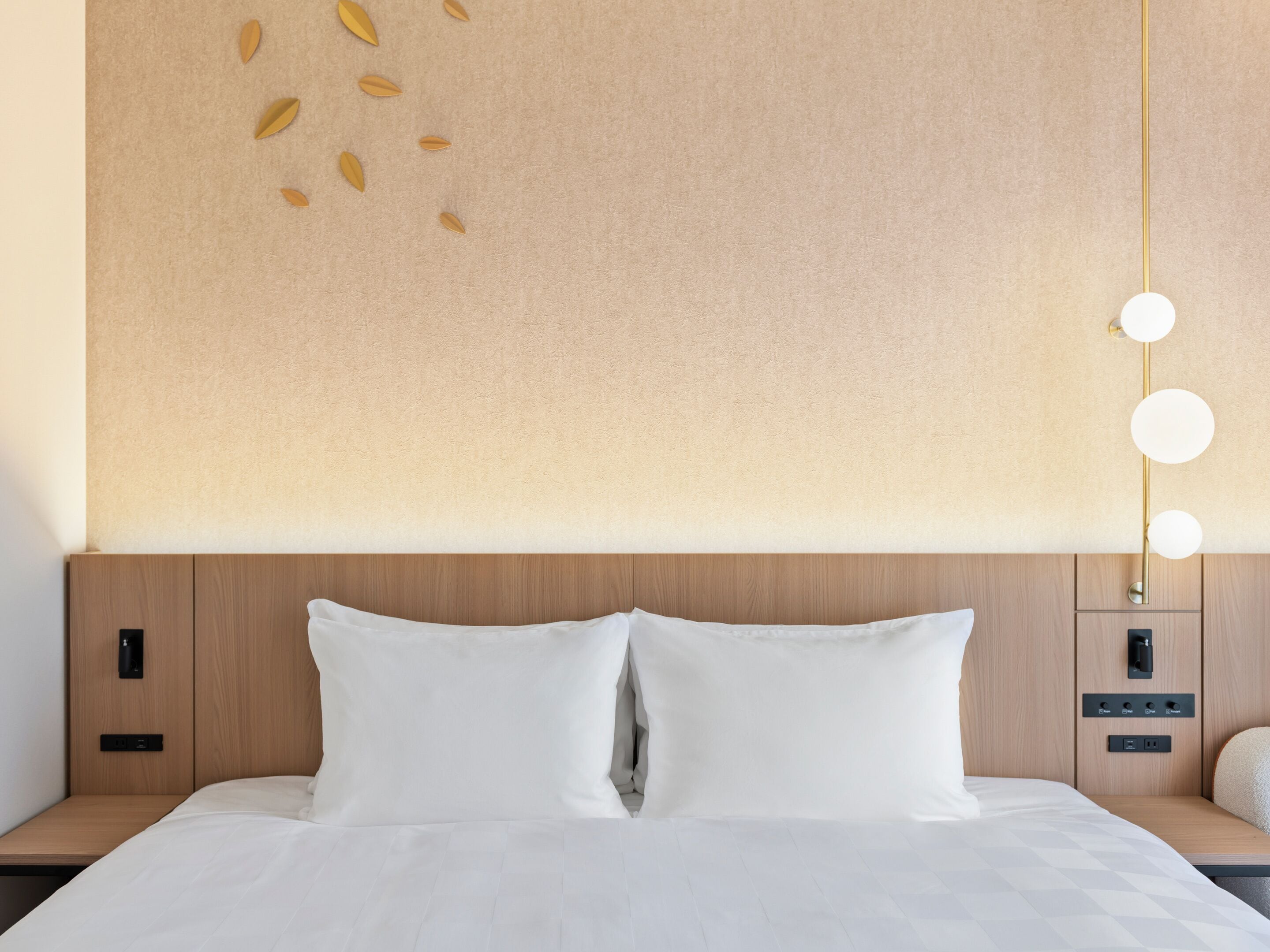 A neatly made bed with white linens, a wooden headboard, and a wall-mounted light fixture with three round bulbs.