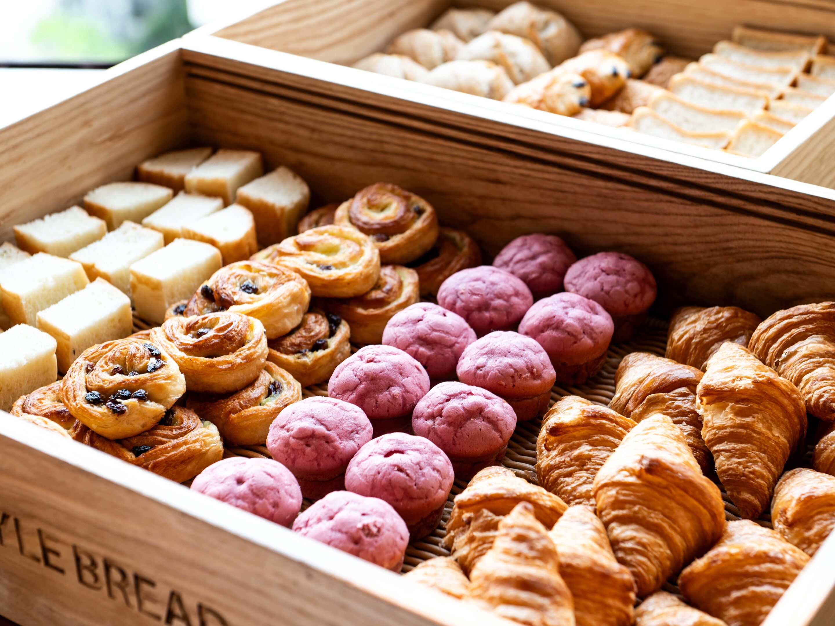 A wooden box filled with various pastries including croissants, muffins, and other baked goods.