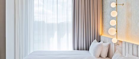 Una habitación de hotel con dos camas, un ventanal con cortinas translúcidas, una lámpara de pared y una pared con textura.