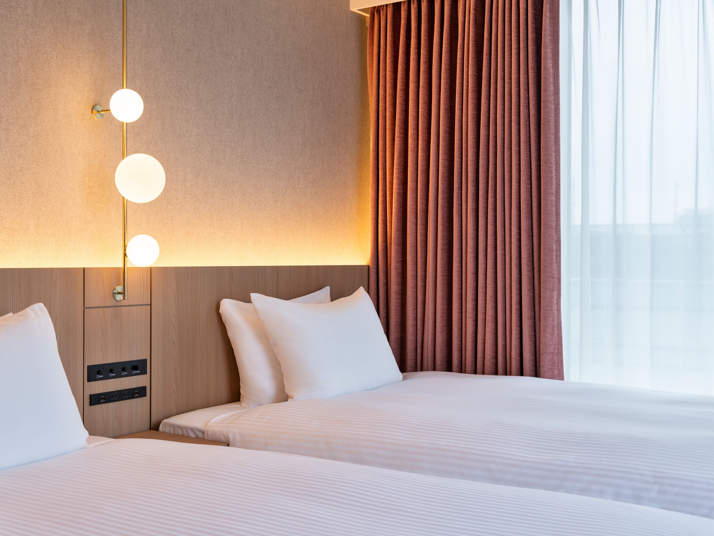Habitación de hotel con dos camas, una lámpara fijada a la pared y una ventana con cortinas.