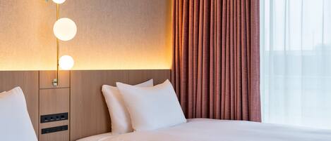 Habitación de hotel con dos camas, una lámpara fijada a la pared y una ventana con cortinas.