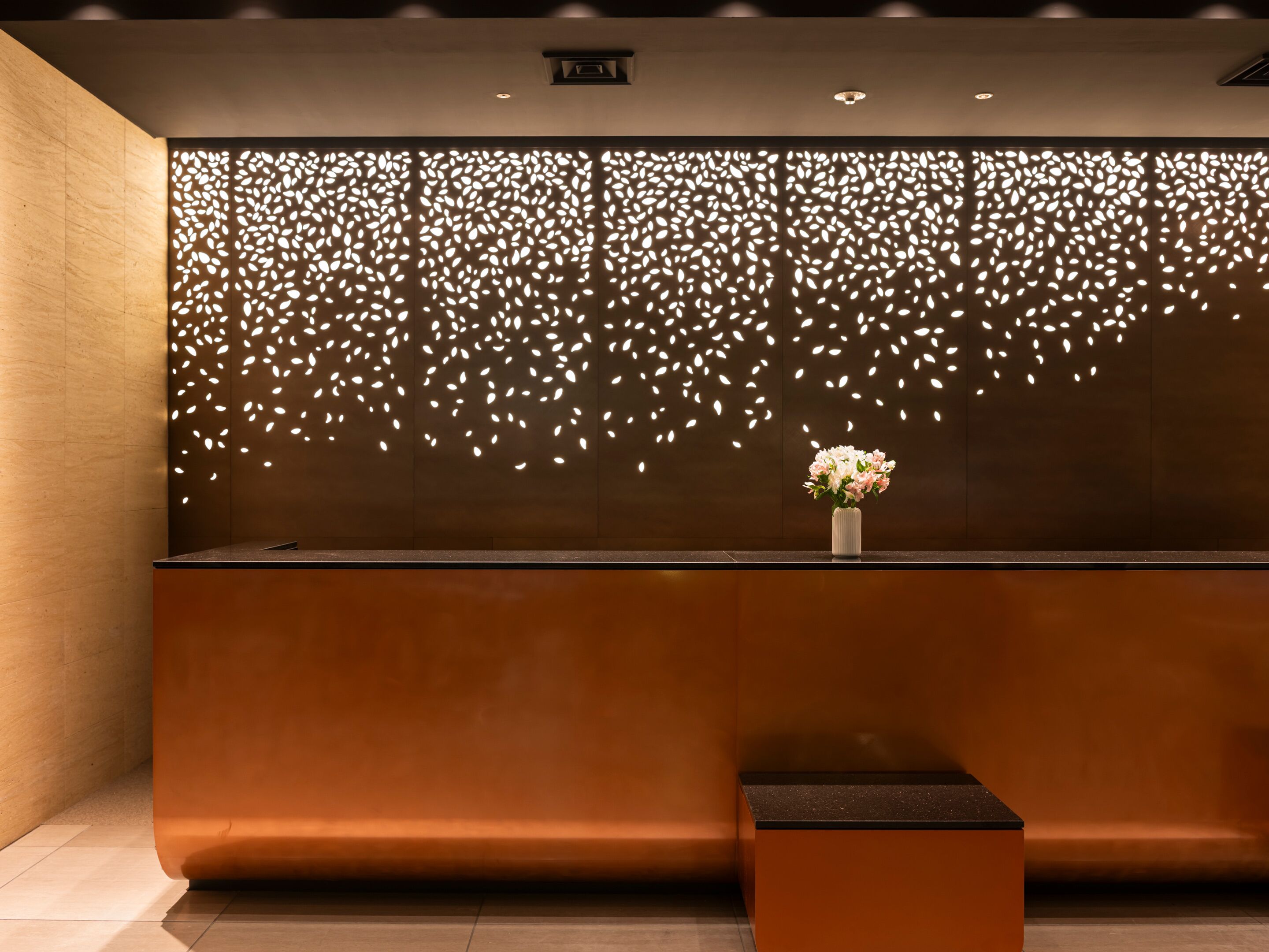 A reception desk with a modern design, featuring a decorative wall with leaf patterns and a vase with flowers.