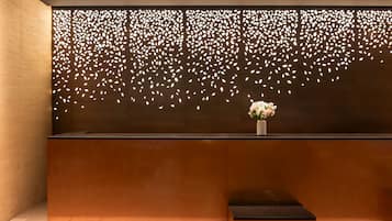 A reception desk with a modern design, featuring a decorative wall with leaf patterns and a vase with flowers.