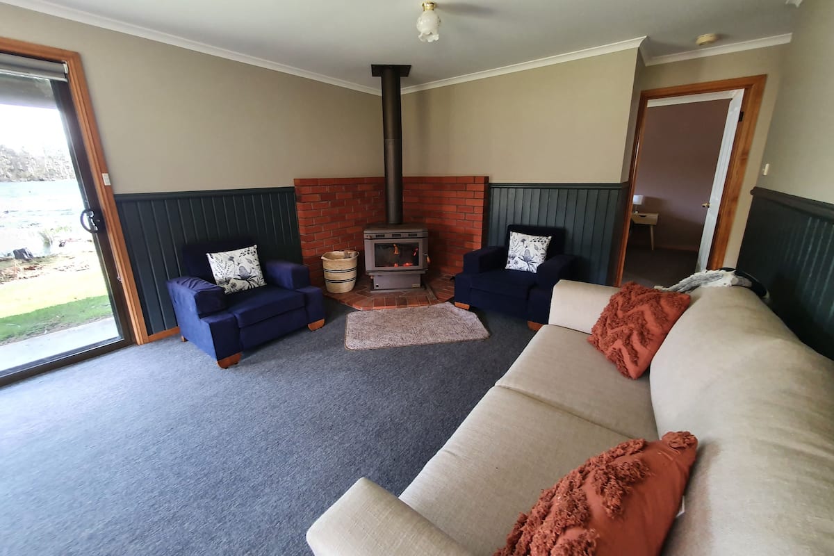 Una sala de estar acogedora con chimenea, dos sofás y un ventanal grande.