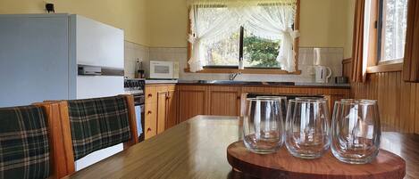 A kitchen with wooden cabinets, a microwave, a stove, and a dining table with four empty glasses.