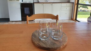 A kitchen with a wooden table, four clear glasses, a window, and a view of greenery outside. - Lake Yalleena Nature Retreat (Lake Leake)